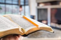 A man holds a Bible with a pencil, against the background of the living room.